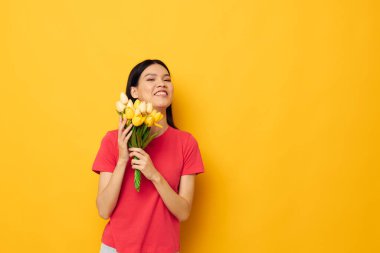 Bir buket çiçekli neşeli Asyalı kız sarı arka planda