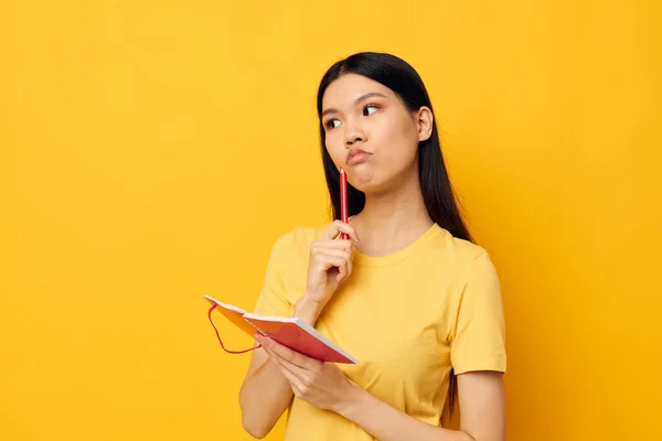 Charmante jeune femme asiatique dans un t-shirt jaune modèle de studio de formation carnet rouge inchangé — Photo