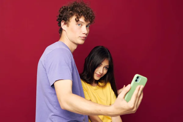 Giovane uomo e ragazza in t-shirt colorate con uno sfondo rosso telefono — Foto Stock