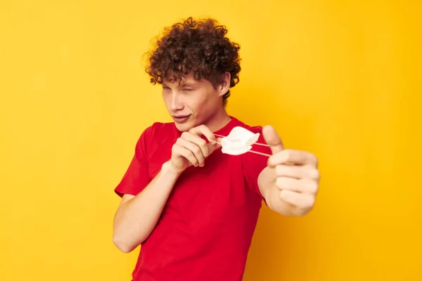Kırmızı tişörtlü genç, kıvırcık bir adamın portresi tıbbi maske koruması sarı arka plan değiştirilmemiş — Stok fotoğraf