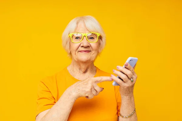 노란색 배경 전화로 가볍게 티셔츠를 입고 대화하는 할머니 — 스톡 사진
