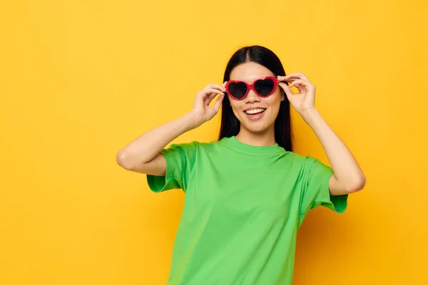 Charmig ung asiatisk kvinna i mörka glasögon i en grön t-shirt poserar modern gul bakgrund oförändrad — Stockfoto