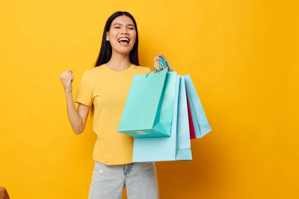 Pretty brunette in a yellow T-shirt with multicolored shopping bags studio model unaltered — Stock Photo, Image