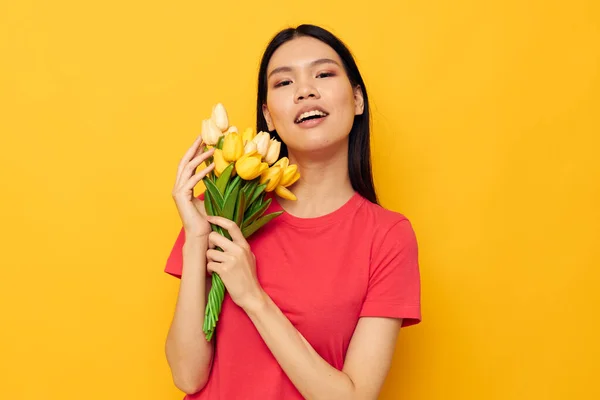 Glad söt asiatisk flicka med en bukett blommor gul bakgrund — Stockfoto