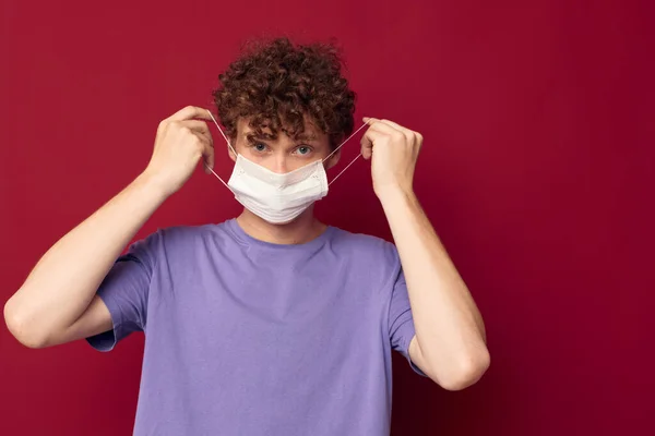 Jovem cara máscara médica proteção posando fundo vermelho inalterado — Fotografia de Stock