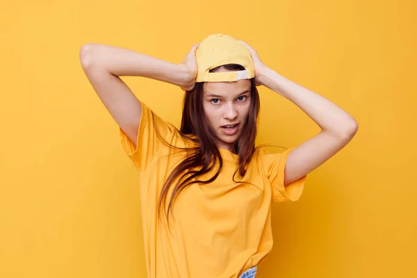 Optimistisk ung kvinna poserar i en gul T-shirt och mössa gul bakgrund — Stockfoto