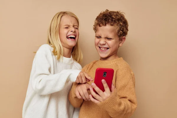 Ragazzino e ragazza con un telefono rosso insieme tecnologie isolato sfondo — Foto Stock