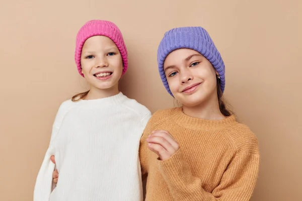 Twee kleine meisjes in truien en hoeden knuffel vriendschap beige achtergrond — Stockfoto