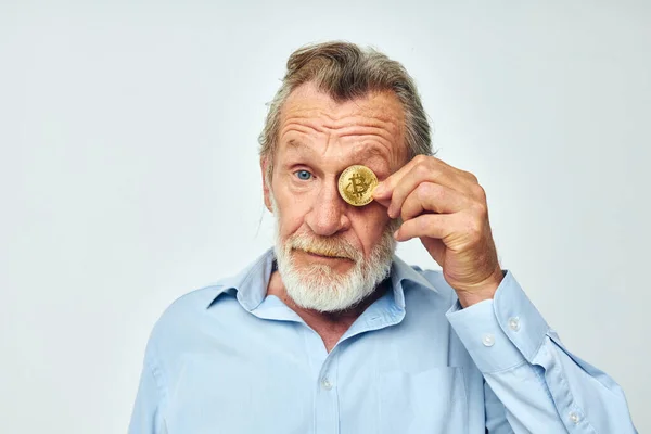 an elderly man in a blue shirt covers the eyes of a bitcoin coin