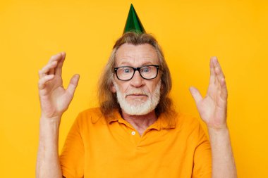 Kafasında şapkası olan sarı tişörtlü yaşlı bir adam. Eğlenceli tek renkli bir fotoğraf.