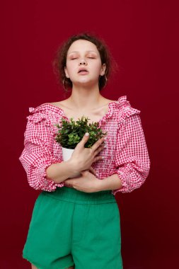 Pembe bluzlu güzel bir kadın beyaz tencerede bir bitkiyle poz veriyor.