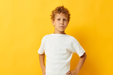 Beyaz tişörtlü neşeli çocuk stüdyo sarısı arka planda poz veriyor.
