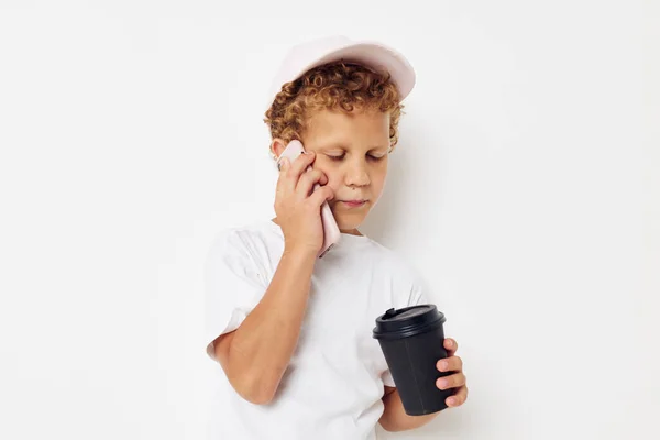 Lindo chico en una gorra de camiseta blanca con un teléfono en un vaso con un estilo de vida de bebida inalterado — Foto de Stock