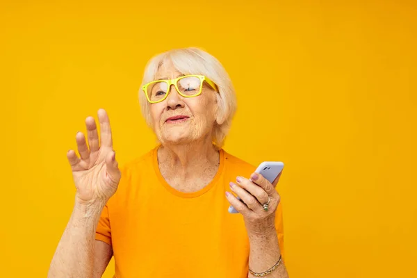 Sonriente anciana feliz estilo de vida en camisetas amarillas con el teléfono de fondo amarillo — Foto de Stock