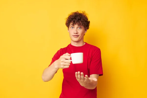 Beyaz kupayla poz veren kıvırcık saçlı genç bir adam ve sarı arka planda değişmemiş bir içeceğin ellerinde. — Stok fotoğraf