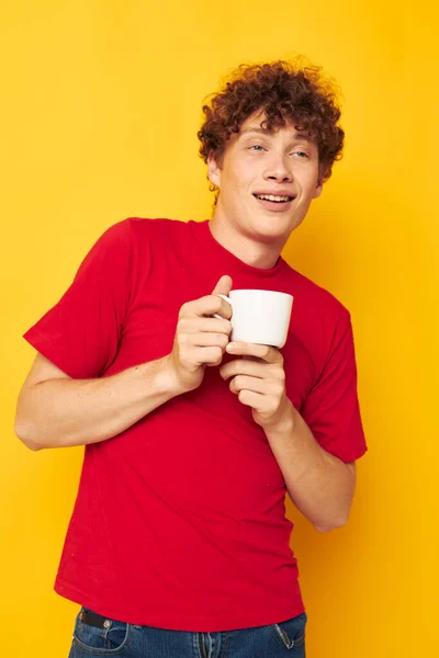 Portrait of a young curly man white mug in the hands of a drink yellow background unaltered — Stockfoto