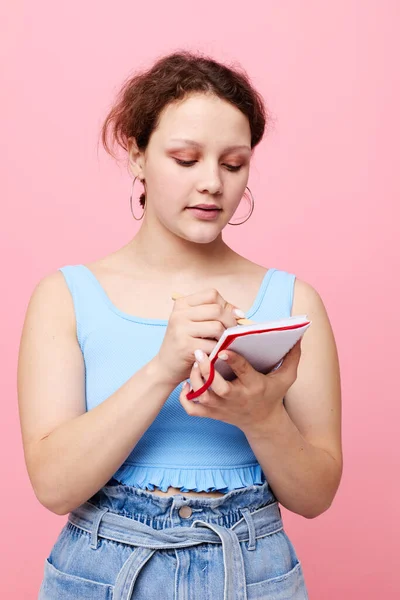 Adolescent fille écriture dans un cahier rouge avec un stylo étude couleur rose fond inchangé — Photo
