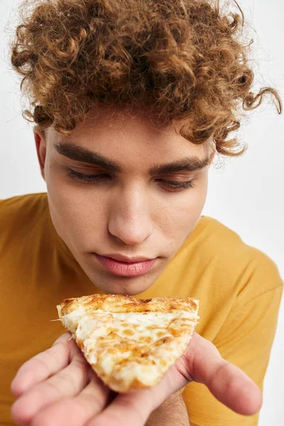 Handsome guy in a yellow t-shirt eating pizza isolated background — Stockfoto