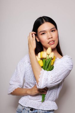 Bir buket çiçekle güzel bir esmer. Gülümse. Kapalı bir arka plan, değiştirilmemiş.