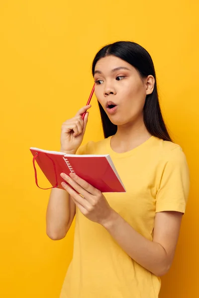 Charmante jeune femme asiatique dans un t-shirt jaune modèle de studio de formation carnet rouge inchangé — Photo