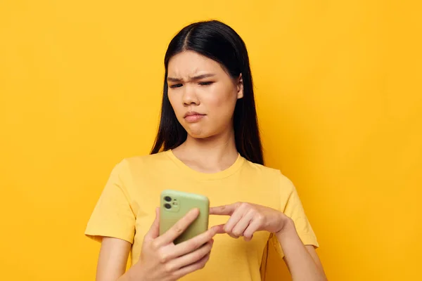 아시아 외모를 하고 있는 여성은 아무런 변화 없이 노란 배경을 가진 전화로 의사소통을 한다 — 스톡 사진