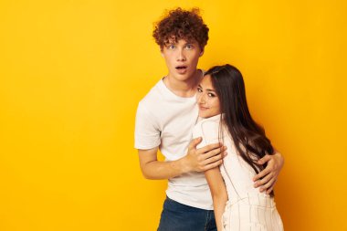 Gençler birbirlerine beyaz tişörtlerle sarılıyorlar. Sarı arka plan değişmemiş.