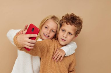 Telefonla izole edilmiş arka planda eğlenmek için poz veren kazaklı iki çocuğun fotoğrafı.