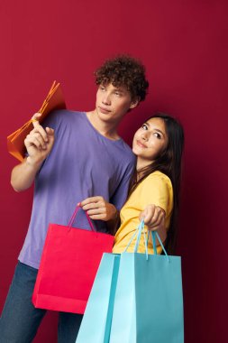 Renkli tişörtlü genç bir çocuk ve kız çantalarla izole edilmiş arka plan alışverişi yapıyorlar.