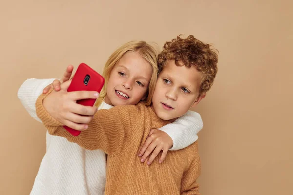 스웨터를 입은 두 어린이가 핸드폰을 사용하여 재미있게 포즈를 취하는 사진 — 스톡 사진