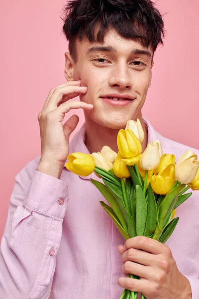 Красивий чоловік в рожевій сорочці з букетом квітів жестикулює своїми руками рожевий фон незмінний — стокове фото