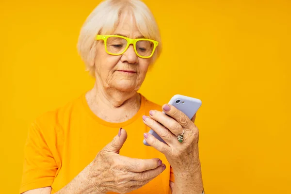 古い友好的な女性の肖像電話技術と黄色のTシャツで幸せな生活 — ストック写真