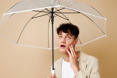 Ceketli, açık şemsiyeli bir adam. Arka planda yağmurdan korunuyor.