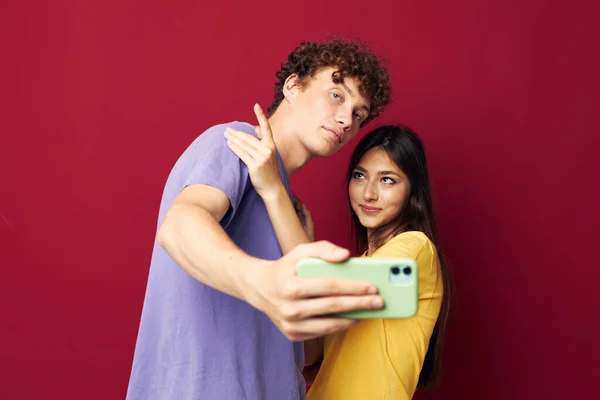 Giovane uomo e ragazza in t-shirt colorate con uno sfondo rosso telefono — Foto Stock