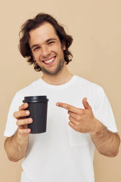 Cheerful man in a white T-shirt with a black glass in hand beige background — Stockfoto