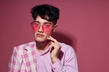 Pembe gözlüklü genç bir adam. Pembe ceketli. Stüdyo pembe arka planda.