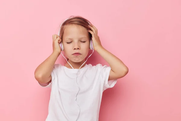 Little girl in a white t-shirt with headphones pink background — Foto Stock