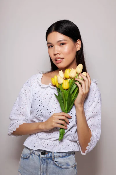 Çiçek buketi olan bir kadın tebessüm eder. Kapalı bir arka plan, değiştirilmemiş.