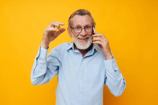 Portrait d'homme âgé heureux dans une chemise bleue et des lunettes parlant sur le téléphone fond jaune — Photo