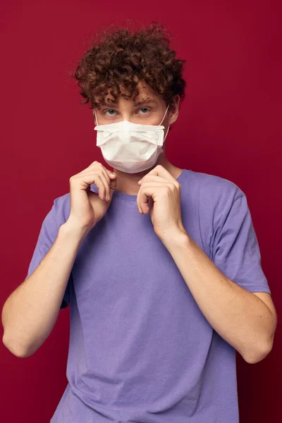 Jovem cara máscara médica proteção posando fundo vermelho inalterado — Fotografia de Stock