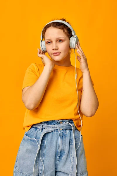 Komik kız kulaklıkla müzik dinliyor. Gençlik tarzı sarı arka plan değiştirilmemiş. — Stok fotoğraf