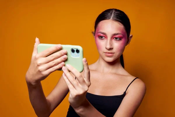 Young beautiful woman looks at the phone bright makeup posing fashion emotions yellow background unaltered — Foto Stock