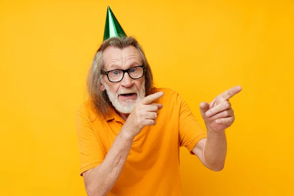 Senior grijs-harige man met een bril groene pet op zijn hoofd vakantie emoties gele achtergrond — Stockfoto