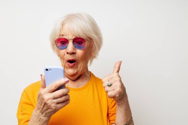 Elinde akıllı bir telefonla şık gözlükler takan yaşlı bir kadın.