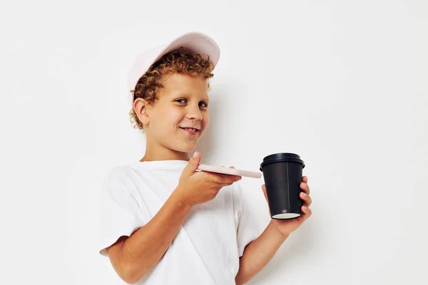 Lindo chico en un blanco camiseta gorra con un teléfono en un vaso con una bebida aislado fondo inalterado — Foto de Stock