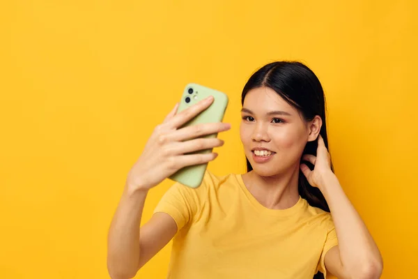 노란 티셔츠를 입고 변경되지 않은 생활 방식을 보여 주는 전화를 보고 있는 아시아의 아름다운 여성 — 스톡 사진