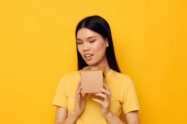 Elinde küçük bir kutu hediye taşıyan kadın. Sarı arka plan.