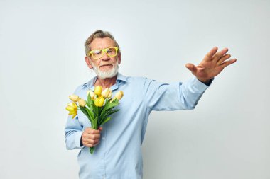 Mavi tişörtlü mutlu yaşlı adamın portresi. Çiçek buketi açık arkaplan.
