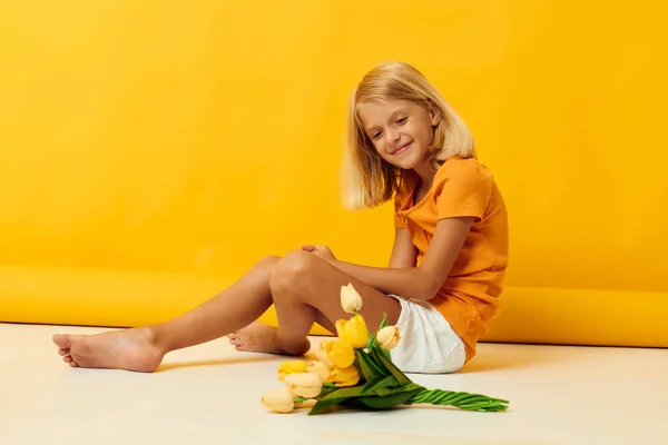 Kislány ül a padlón egy csokor virág sárga háttér — Stock Fotó