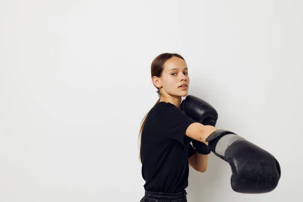 Jonge vrouw in bokshandschoenen in zwarte broek en een T-shirt lichte achtergrond — Stockfoto