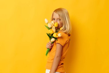 little girl with blond hair with a bouquet of yellow flowers on a yellow background